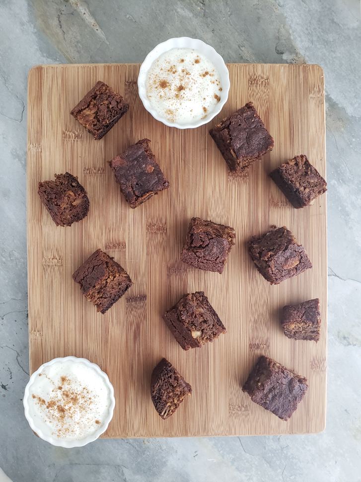 A cutting board with bite-sized chocolate bread bites and two cups of dipping sauce.