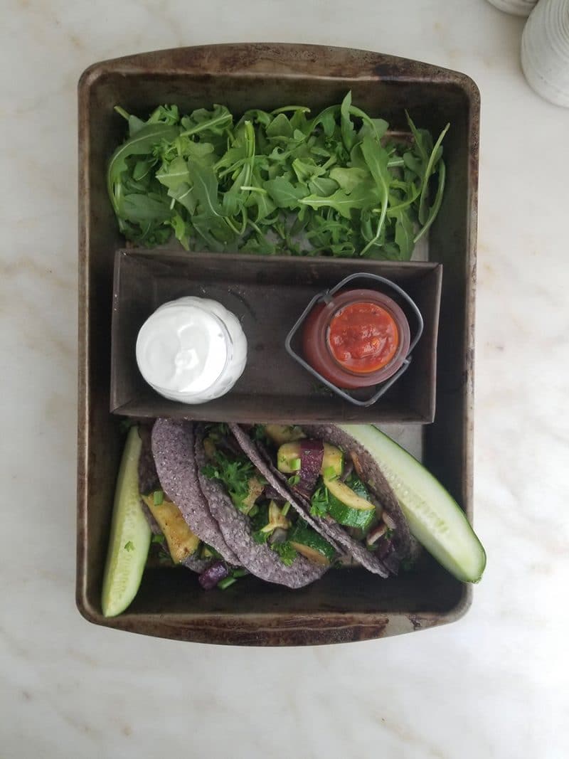 A spread of clean-eating tacos, dips, pickles, and arugula in a baking tray.