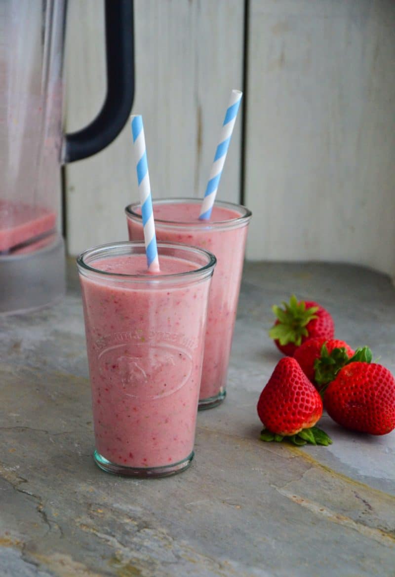 Two strawberry smoothies with straws and strawberry on the side