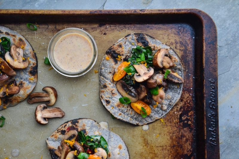 A zoomed in view of gluten-free veggie fajitas with a dairy-free sauce on the side on top of a baking sheet.