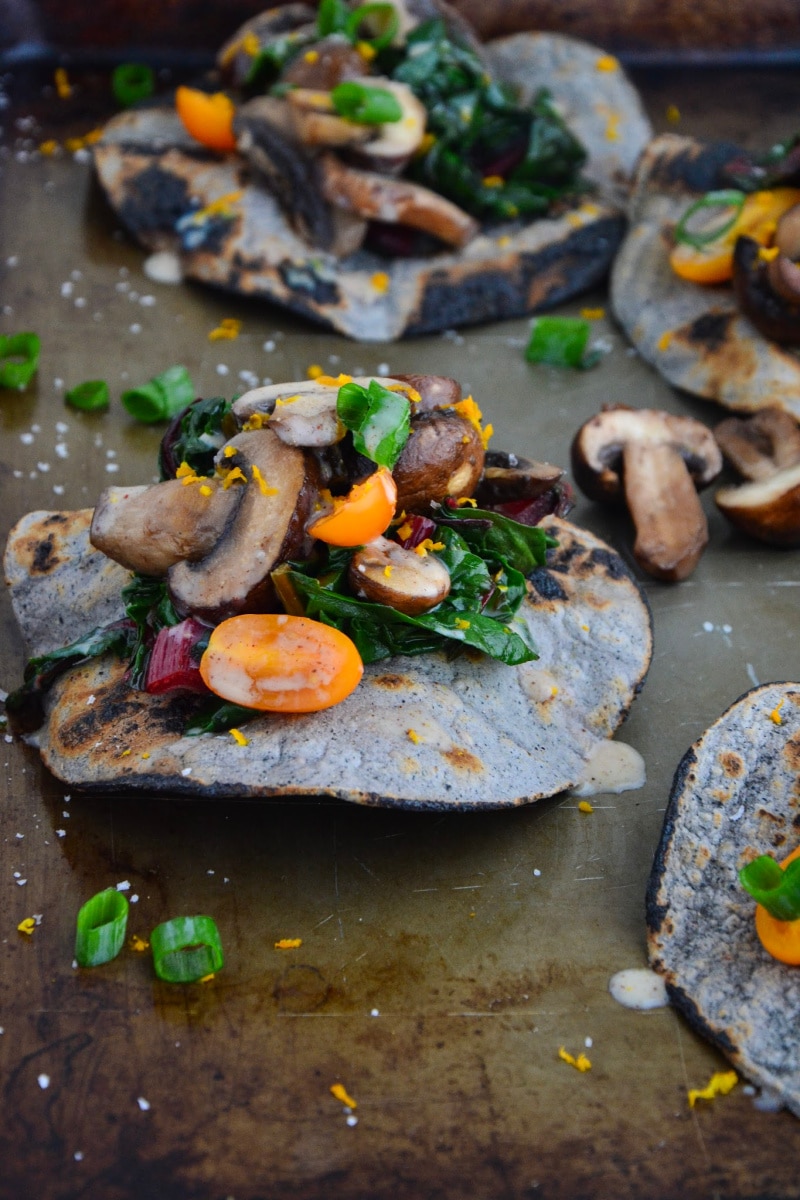 Gluten-free fajita topped with organic mushrooms, Swiss chard and tomatoes on a baking sheet.