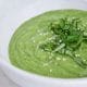 A bright green pureed soup in a serving-size white bowl, topped with sesame seeds.