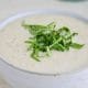 A white bowl with a creamy white soup and topped with greens.