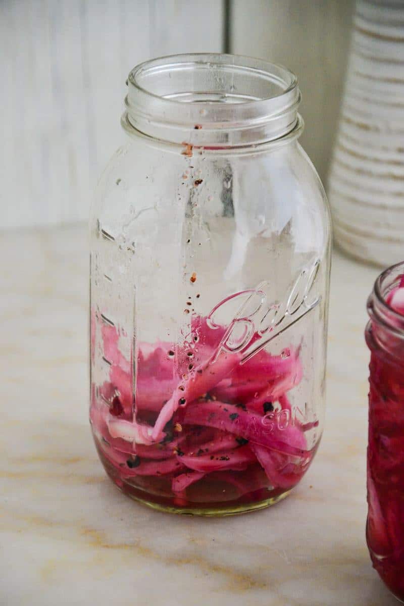 A large mason jar about 1/3 full of bright pink red onions.