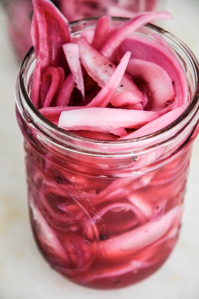 A close up of a mason jar full of thinly sliced onion in a bright pink pickling juice.