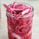 A mason jar full of beautiful red pickled onions.