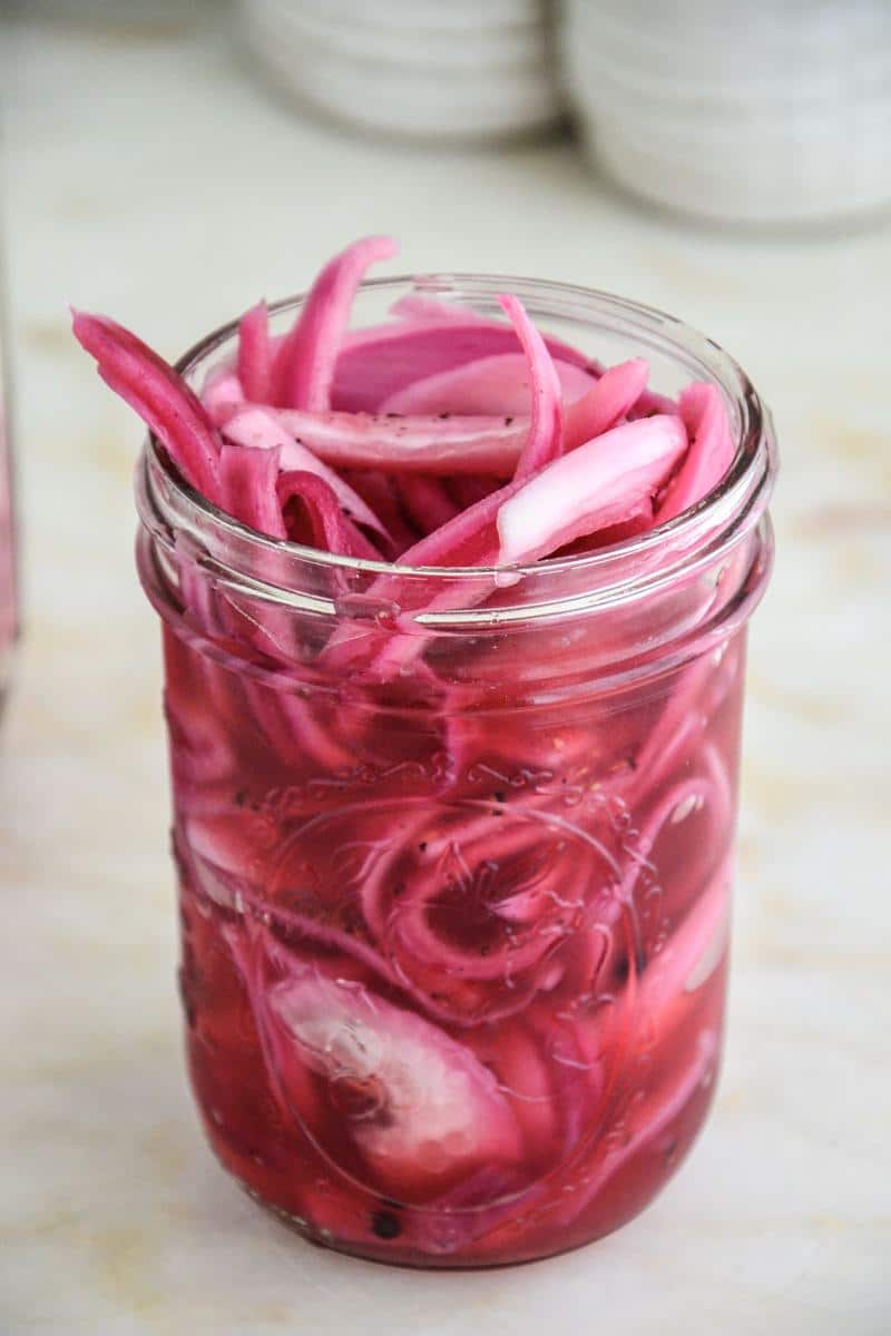 A mason jar full of beautiful red pickled onions.
