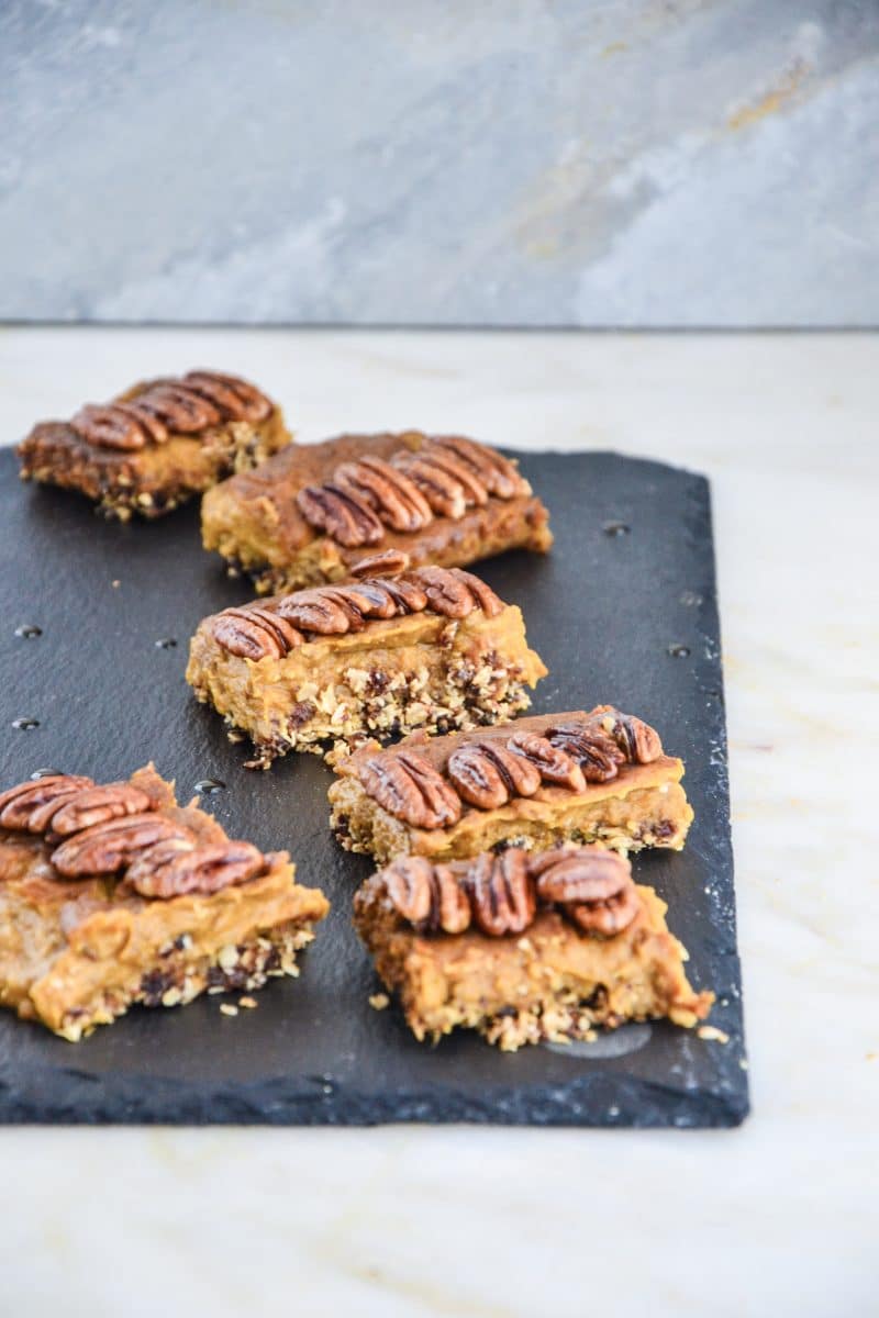 Delicious gooey pumpkin pie treats on top of a crumbly oatmeal crust, cut into squares, on a slate.
