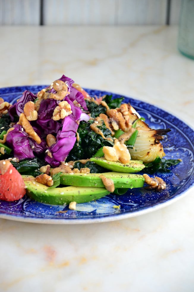 Easy massaged kale salad on a blue plate with avocado, grapefruit and walnuts.