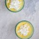Easy Mango Pudding recipe that's topped with coconut flakes in beautiful glasses on a marble table.
