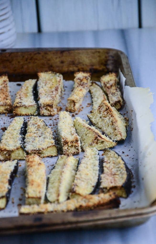 Eggplant fries on rimmed baking sheets on a marble table.