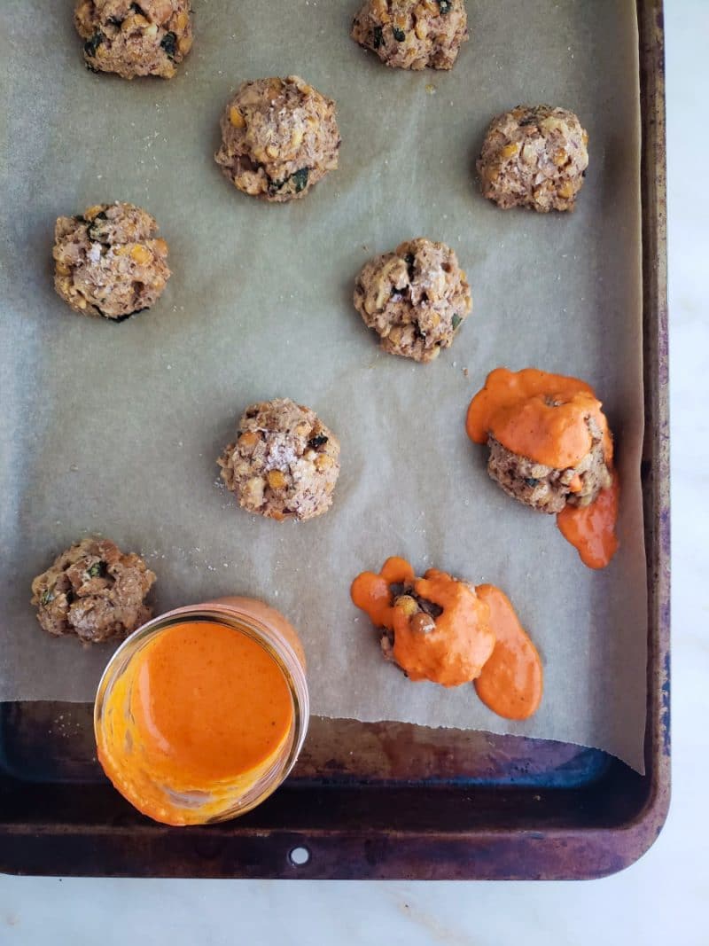 Gluten free chickpea beanballs on parchment paper on a baking sheet with orange sauce.