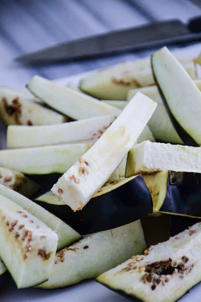 Sliced eggplant fries on a marble table ready to be coated with almond flour.