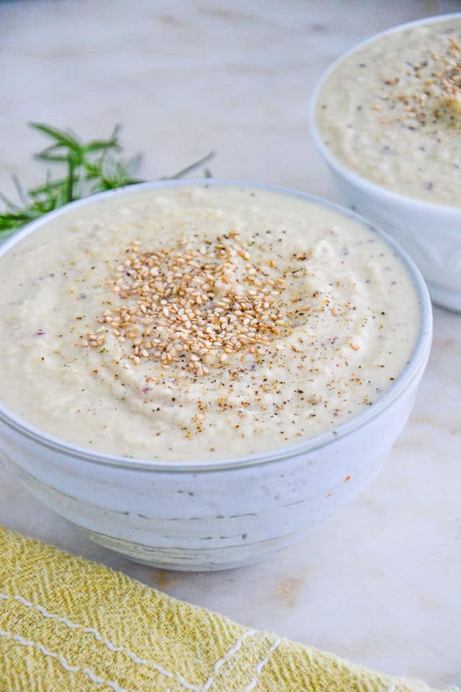 Creamy Vegan Cauliflower Soup in a light blue bowl on a marble table top with sesame seeds.