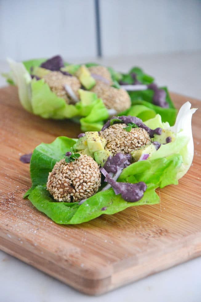 Gluten-Free Falafel in a large lettuce leaf with a cherry tahini vegan falafel dressing on a wooden serving board.