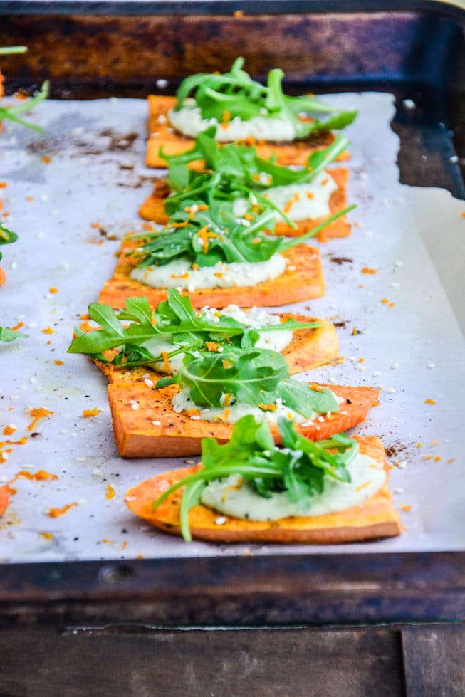 Roasted Sweet Potato Appetizer with dairy-free cream and arugula on top on a baking sheet.