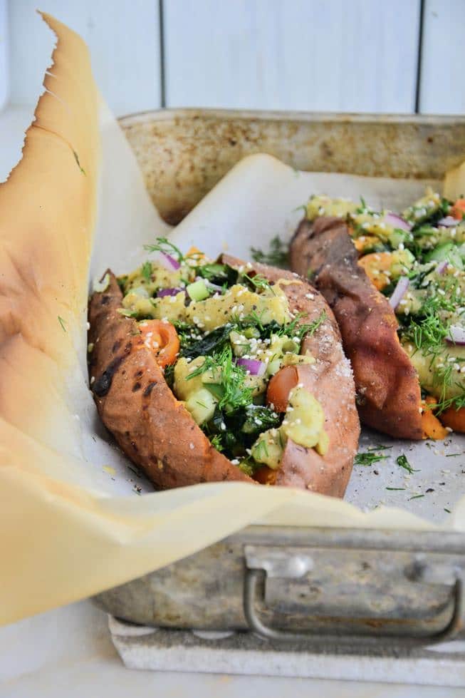 Healthy Oven Roasted Sweet Potatoes stuffed with vegetables and a creamy sauce in a baking dish with parchment paper.