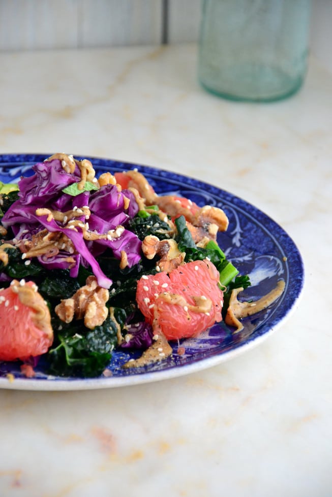 Sweet roasted onions in a massaged kale avocado salad on a blue plate with creamy almond dressing.