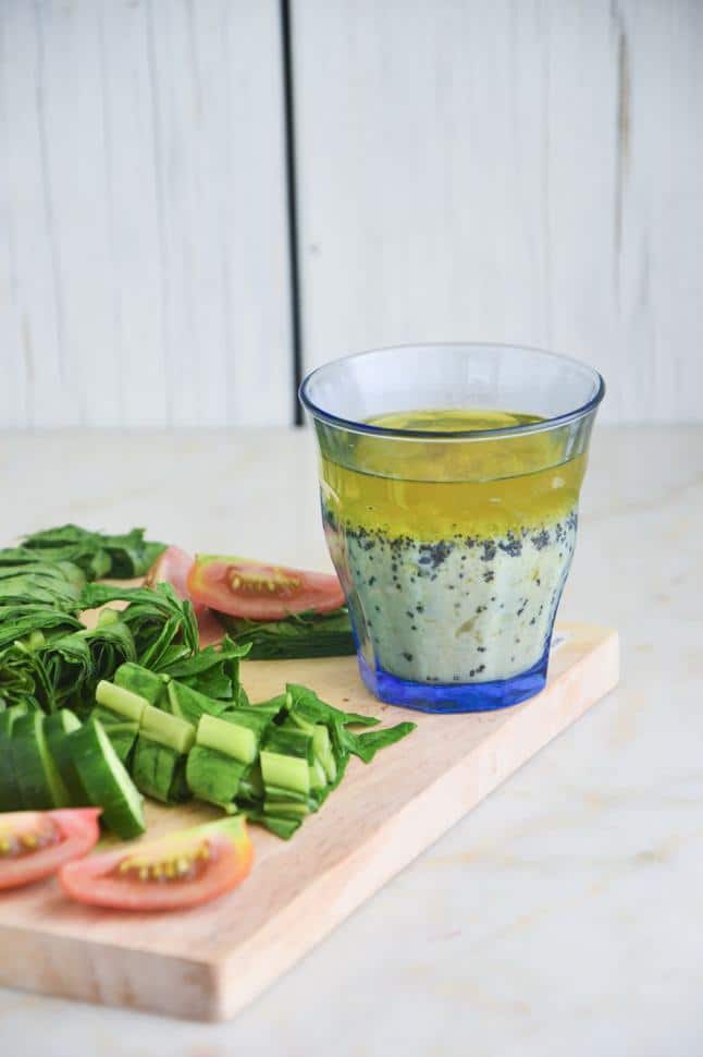 Lemon poppy seed dressing in a cup on a cutting board with chopped fresh veggies.
