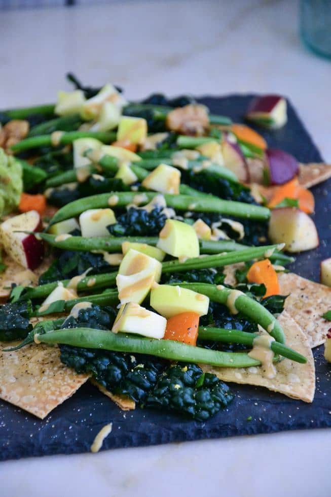 The best veggie nachos filled with kale and other veggies and homemade tortilla chips on a slate.