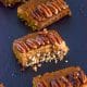 Four pumpkin pie squares with crumbly crust and pecans on top on a board.