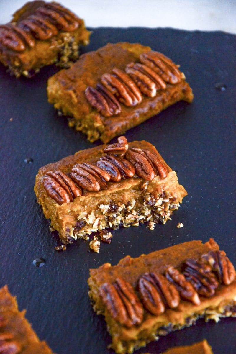 Four pumpkin pie squares with crumbly crust and pecans on top on a board.