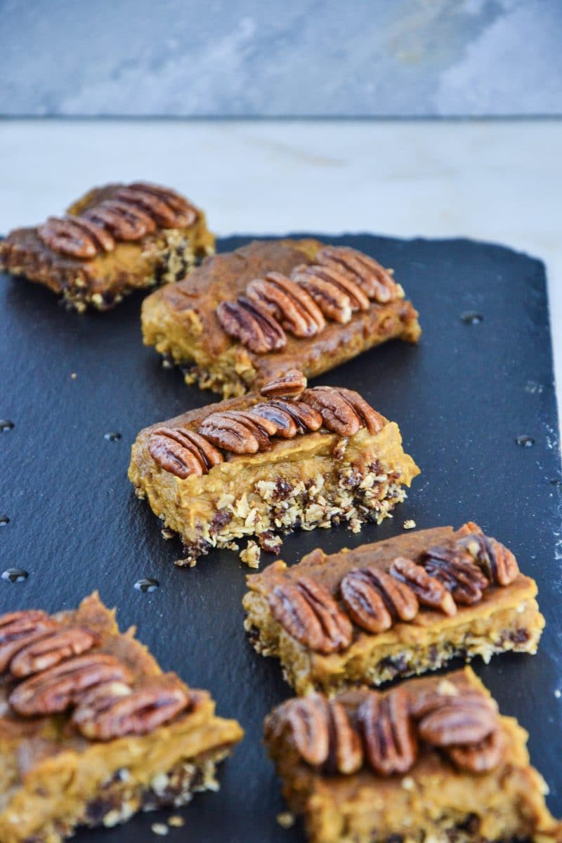 A bunch of square pumpkin pie bites topped with pecans sitting on a counter.