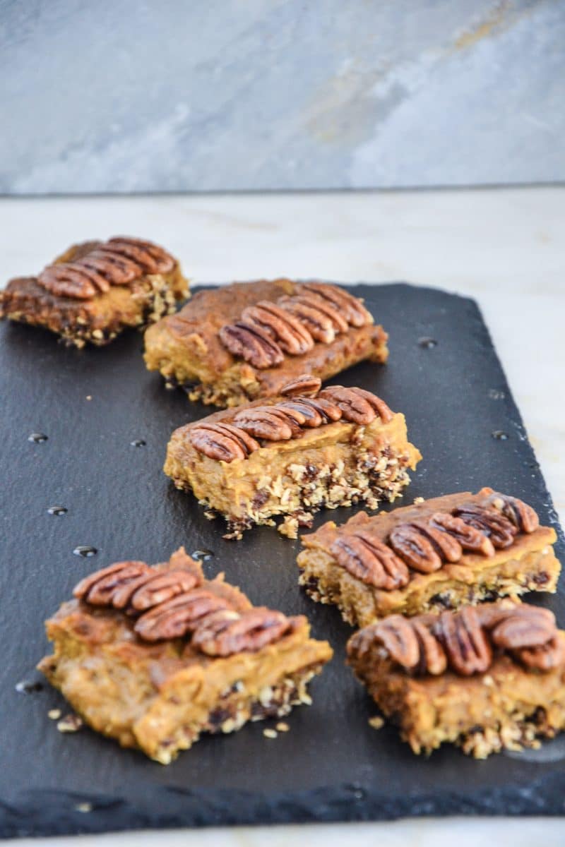 Pumpkin spice pie bars on a slate topped with four pecans each.