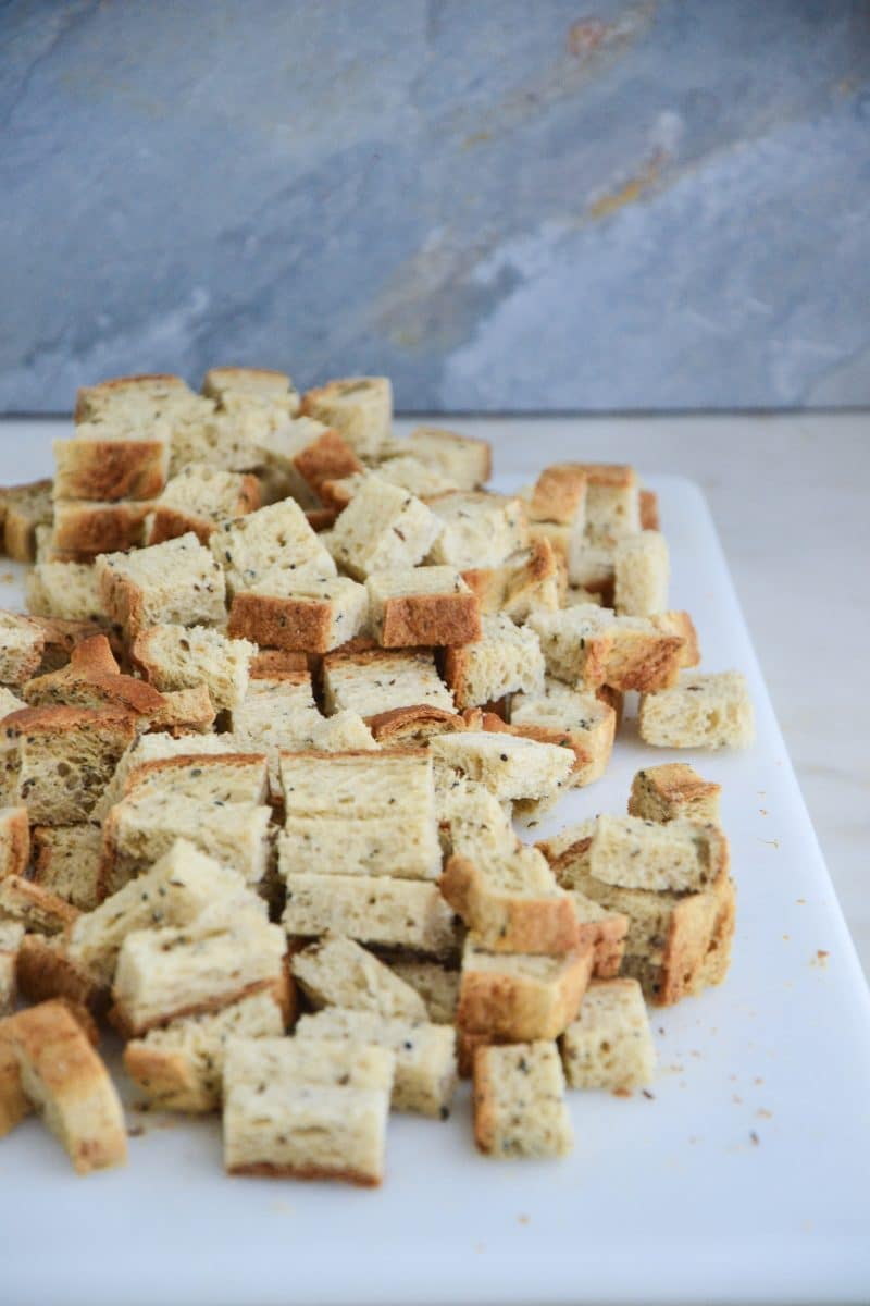 Bread diced into small cubes on a cutting board.