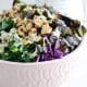 Delicious kale salad with tahini dressing, walnuts, figs and red cabbage in a pink bowl on marble.