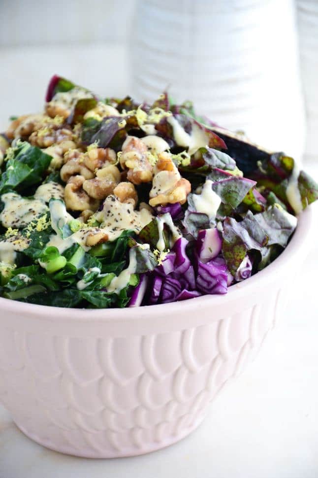 Delicious kale salad with tahini dressing, walnuts, figs and red cabbage in a pink bowl on marble.