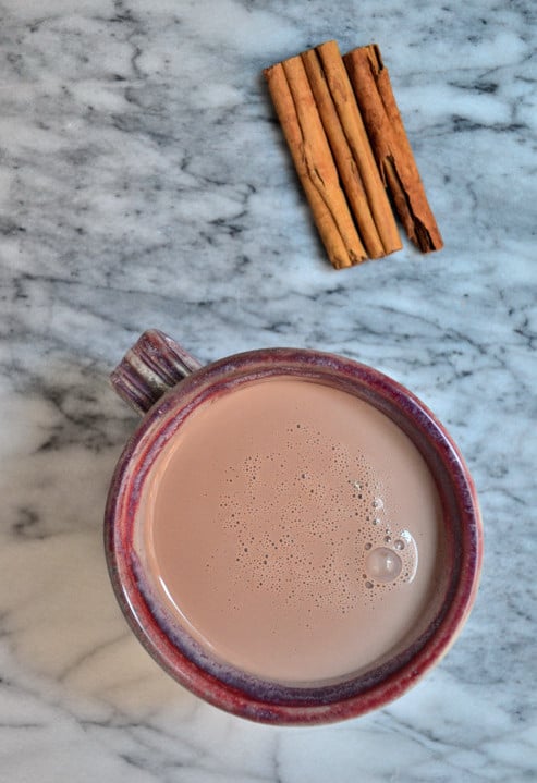 An overhead image of a mug of hot cocoa on a counter with some cinnamon sticks.