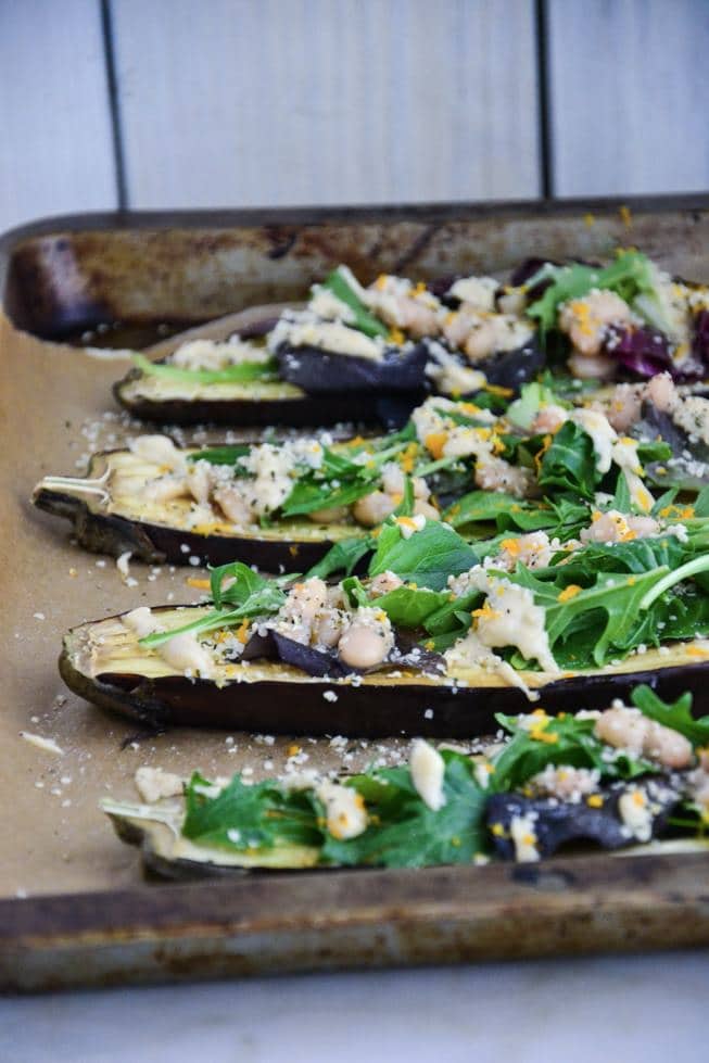 Roasted eggplant with arugula on top and hemp seeds on a baking sheet.