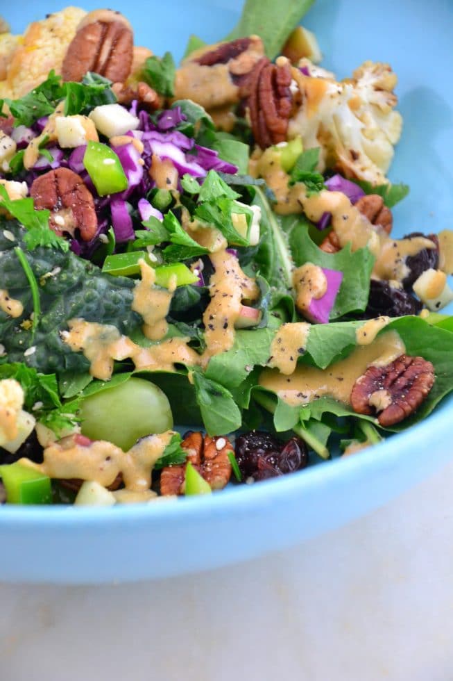 A beautiful blue bowl on a marble table top filled with kale salad and tahini dressing.