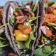 Gorgeous tacos stacked together and filled with green arugula, orange and yellow carrots, and perfectly carmelized onions.
