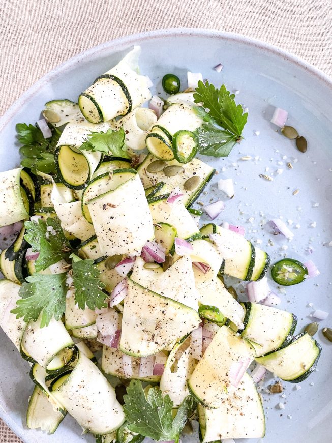 A salad of pale green zucchini ribbons, bright green herbs and jalapenos, and pops of pink red onion.